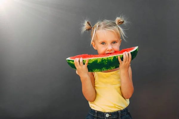 Забавный ребенок ест арбуз на открытом воздухе на сером фоне . — стоковое фото
