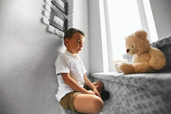 Little boy is hugging a teddy bear, smiling while sitting on st — Stock Photo, Image