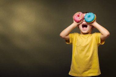 Mutlu şirin çocuk siyah arka plan duvarında çöreklerle oynarken eğleniyor. Bir çocuğun parlak fotoğrafı. Renkli çörekler