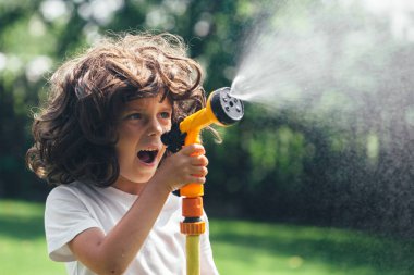 Çocuk bahçede suyla oynuyor.