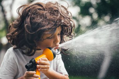 Çocuk bahçede suyla oynuyor.