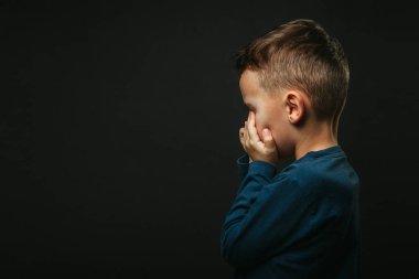 Depresyonu siyah arka planda elleri kapalı bir çocuk.
