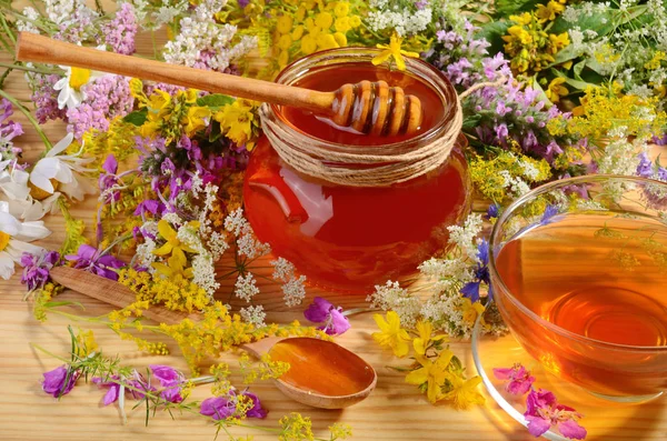 在花背景上木桌上喝茶的蜂蜜玻璃罐 — 图库照片