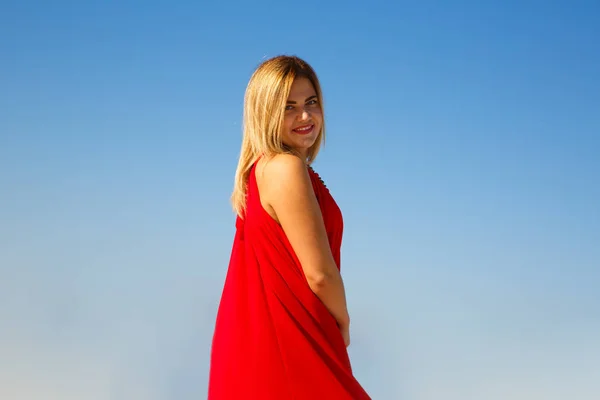 蓝色天空背景的红色礼服的金发女郎 — 图库照片