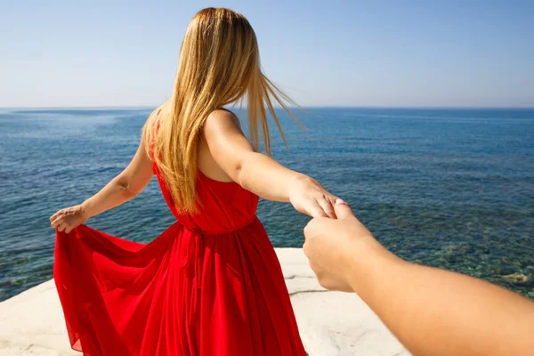 付いて来てください キプロスのビーチで友人の手を握って 赤いドレスの若いブロンドの女性 — ストック写真