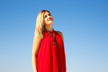 Mavi gökyüzü arka plan üzerinde Kırmızı elbiseli sarışın kadın.