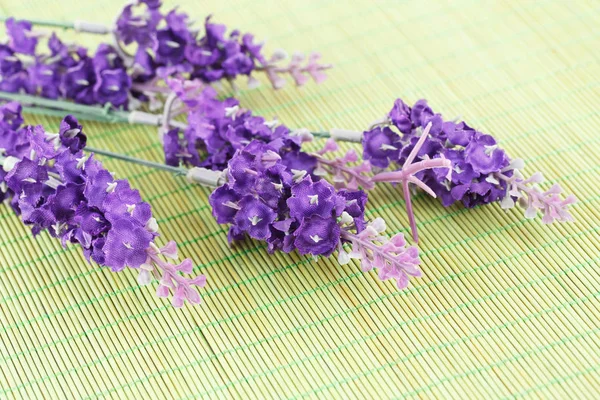 Violet fabric flowers on bamboo background, closeup picture.