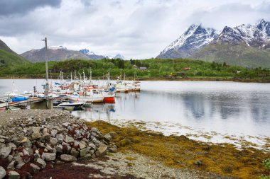 Yüksek karlı dağlar, köy ve Norveç'te tekne ile küçük liman manzara.