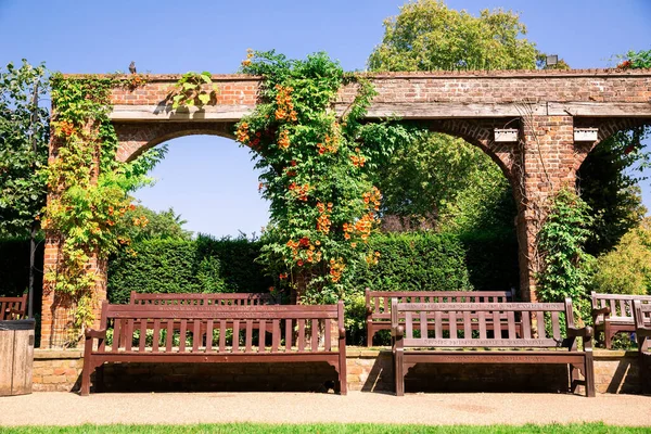 ロンドン 8月26 2019 夏にオランダ公園で花とレンガ造りのアーチで木製の茶色のベンチ — ストック写真