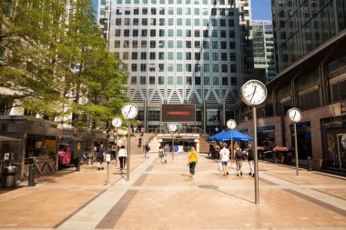 Londra, İngiltere - 26 Ağustos 2019 - Canary Wharf finans bölgesi şirket binaları ve saatleriyle. İş alanında yürüyen insanlar.