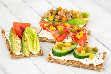 Kraker, peynir, ton balığı ve sebzeli sandviçler gri ahşap arka planda..