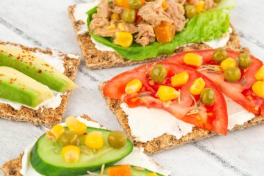 Kraker, peynir, ton balığı ve sebzeli sandviçler gri ahşap arka planda..