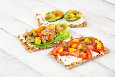 Kraker, peynir, ton balığı ve sebzeli sandviçler gri ahşap arka planda..