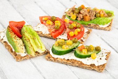 Kraker, peynir, ton balığı ve sebzeli sandviçler gri ahşap arka planda..