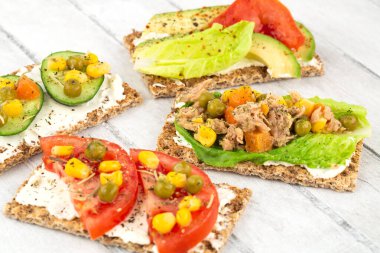 Kraker, peynir, ton balığı ve sebzeli sandviçler gri ahşap arka planda..