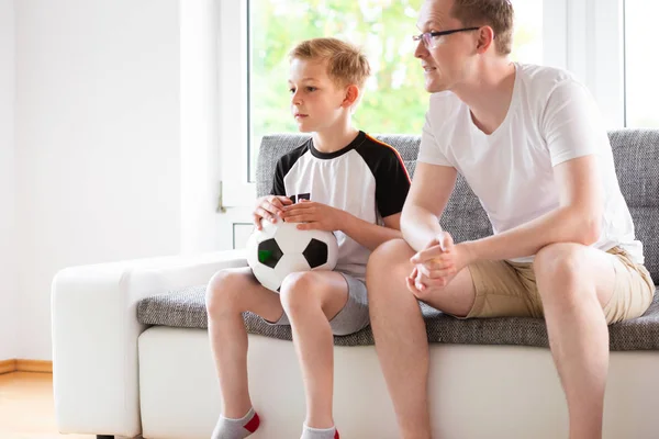 Young father and his son watching world soccer championship with ball on the sofa