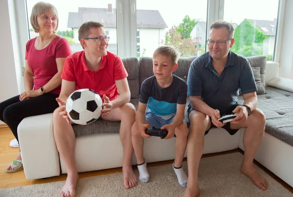 Grandparents, their son and grandson are playing computer game  emotionally at home on sofa