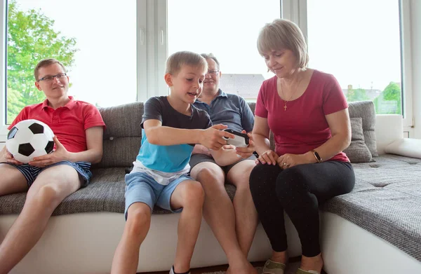 Grandparents, their son and grandson are playing computer game  emotionally at home on sofa