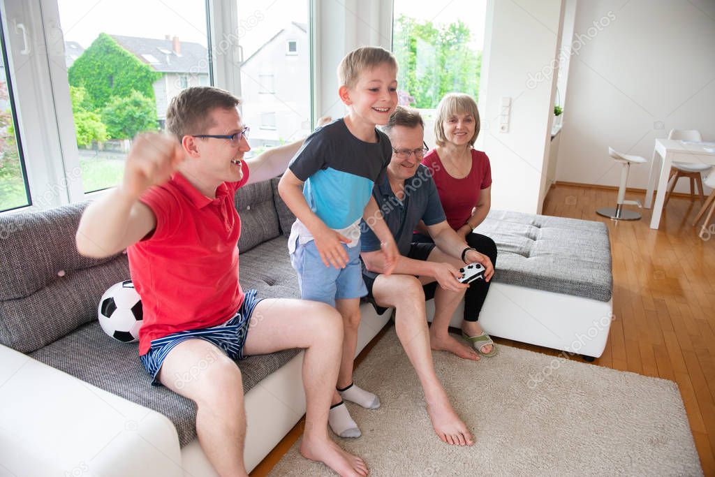  Grandparents, their son and grandson are playing computer game  emotionally at home on sofa