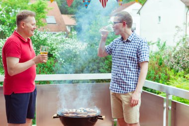 Mutlu arkadaşlar eğlenmeye ve onların konuşma ve içecekler bira sırasında ızgara et ve sebze teras keyfini çıkarın