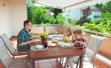 Genç ve mutlu bir aile kahvaltıda büyük teraslarda eğleniyor. 