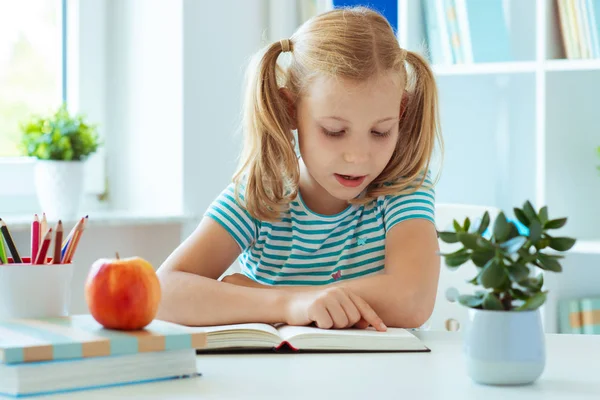 一个可爱的小女孩的肖像看书在光教室的桌子上 — 图库照片