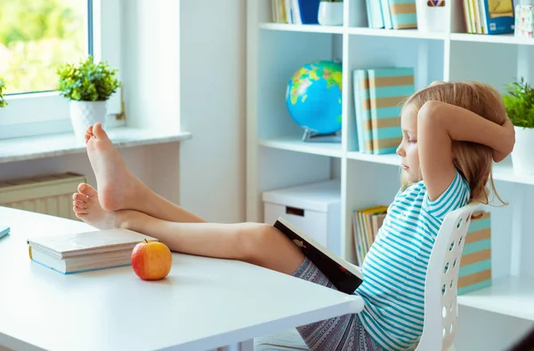 リラックスできる面白い小さな学校の女の子の肖像画は自宅の明るい部屋のテーブルで本を読む — ストック写真