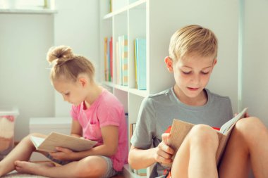 İki mutlu çocuk yerde okul Kütüphanesi'nde kitap okuma