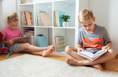 İki mutlu çocuk yerde okul Kütüphanesi'nde kitap okuma