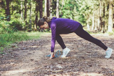 Genç ve güzel bir kadın güneşli ormanda koşuyor ve egzersiz yapıyor.