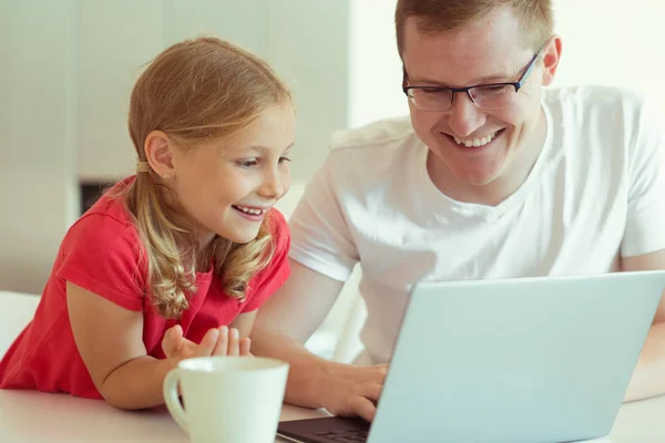 愉快的年轻的父亲有乐趣与他漂亮的小女儿在工作与笔记本电脑在现代家庭 — 图库照片