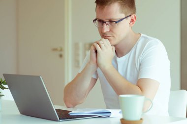 Genç ve yakışıklı adam evde dizüstü bilgisayarıyla çalışıyor. 