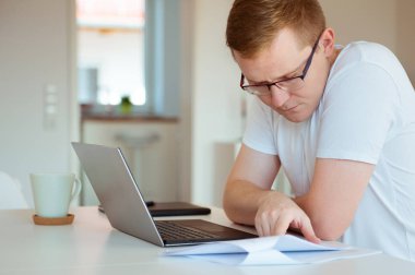 Genç ve yakışıklı adam evde dizüstü bilgisayarıyla çalışıyor.