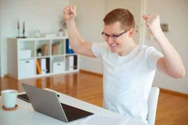 Genç ve yakışıklı adam evde dizüstü bilgisayarıyla çalışıyor.