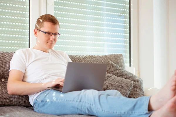 年轻英俊的男人在家里工作 他的笔记本电脑在沙发上 — 图库照片