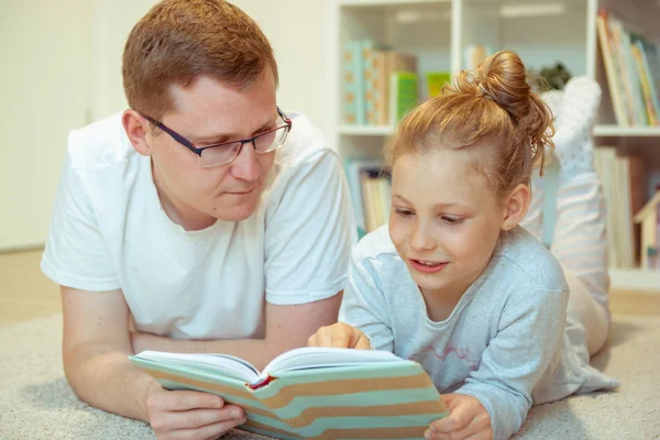 Młody szczęśliwy ojciec czyta książkę z uroczą córką w domu — Zdjęcie stockowe