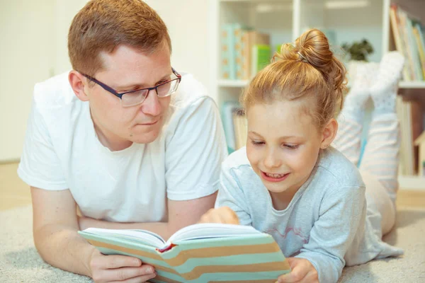 Νεαρός ευτυχισμένος πατέρας ανάγνωση βιβλίο με χαριτωμένο κόρη στο σπίτι — Φωτογραφία Αρχείου
