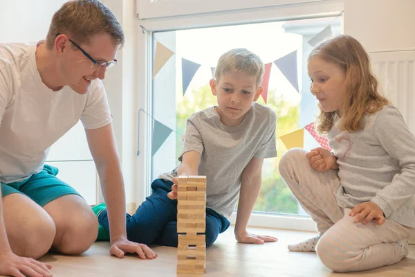 Junger glücklicher Vater spielt mit seinen zwei süßen Kindern mit Holz — Stockfoto