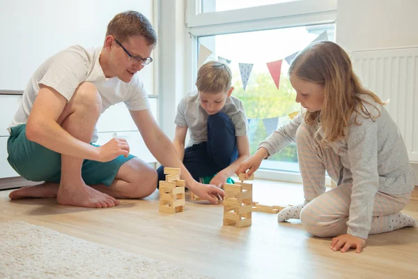 Junger glücklicher Vater spielt mit seinen zwei süßen Kindern mit Holz — Stockfoto