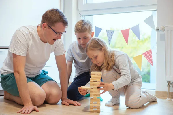 Junger glücklicher Vater spielt mit seinen zwei süßen Kindern mit Holz Stockbild