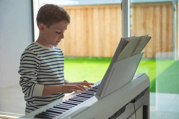 Мальчик-подросток обучается игре на электронном фортепиано дома — стоковое фото