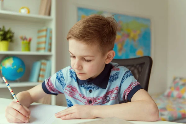 Pequeno menino da escola inteligente fazendo lição de casa na mesa no quarto — Fotografia de Stock