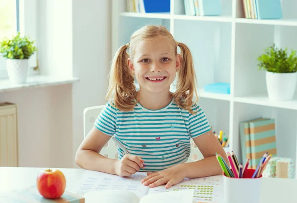 Porträt eines süßen Schulmädchens, das am weißen Tisch bei Licht sitzt — Stockfoto