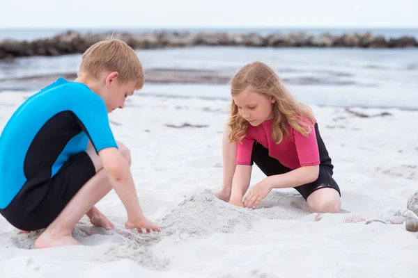 Due bambini in costume da bagno in neoprene che giocano in spiaggia con san — Foto Stock