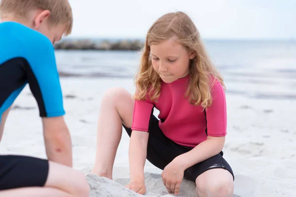 Dos niños en trajes de baño de neopreno jugando en la playa con san — Foto de Stock