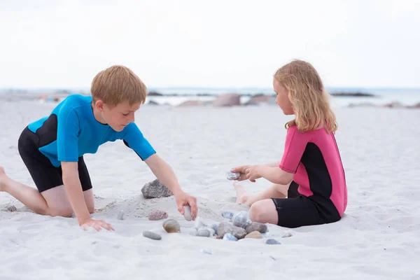 Dos niños en trajes de baño de neopreno jugando en la playa con san — Foto de Stock