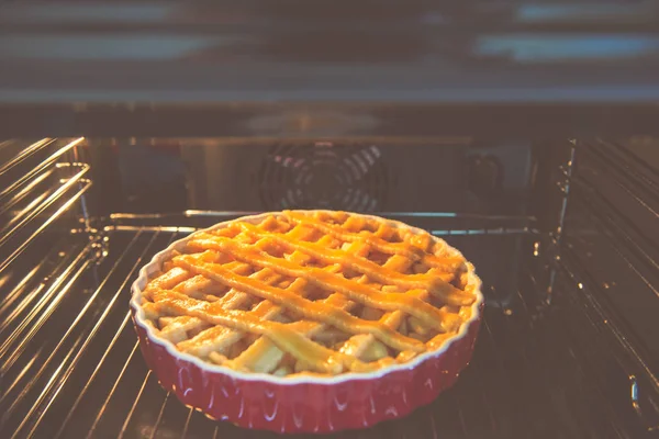 Fresh baked golden apple pie in red dish in oven at kitchen — Stock Photo, Image