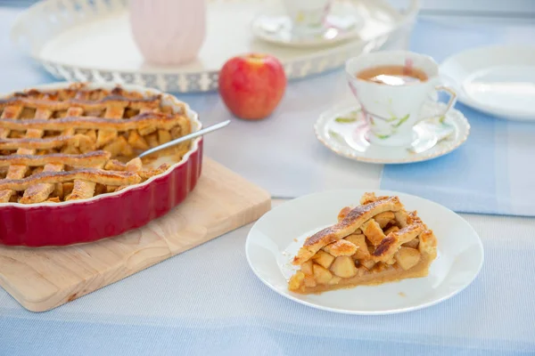 Fresh baked apple pie, cup of tea and flowers on a table