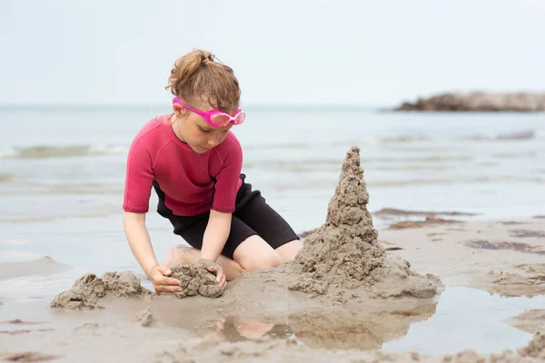 Досить маленька дівчинка в неопренових купальниках грає з піском на місці — стокове фото
