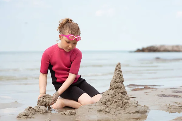 Pretty little girl in neoprene swimsuits playing with sand in se — Stock Photo, Image